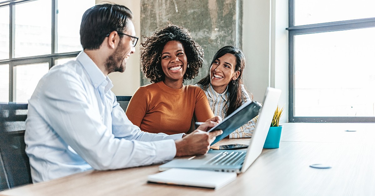 Três pessoas sorrindo em um ambiente corporativo