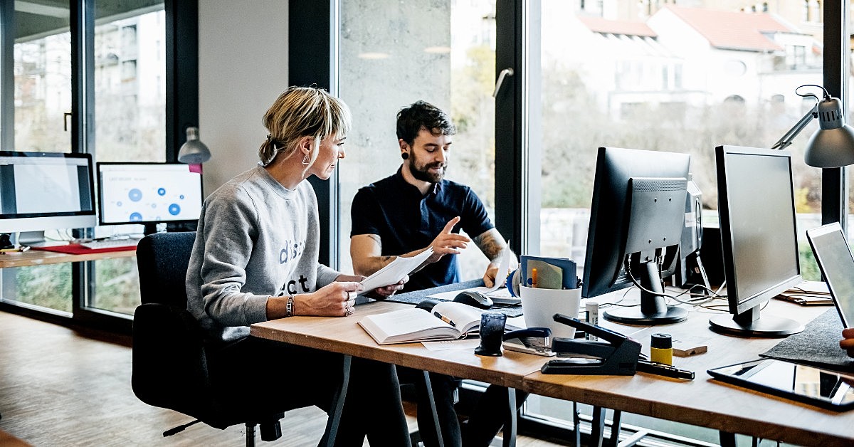 duas pessoas olhando para a tela de um computador em um ambiente corporativo