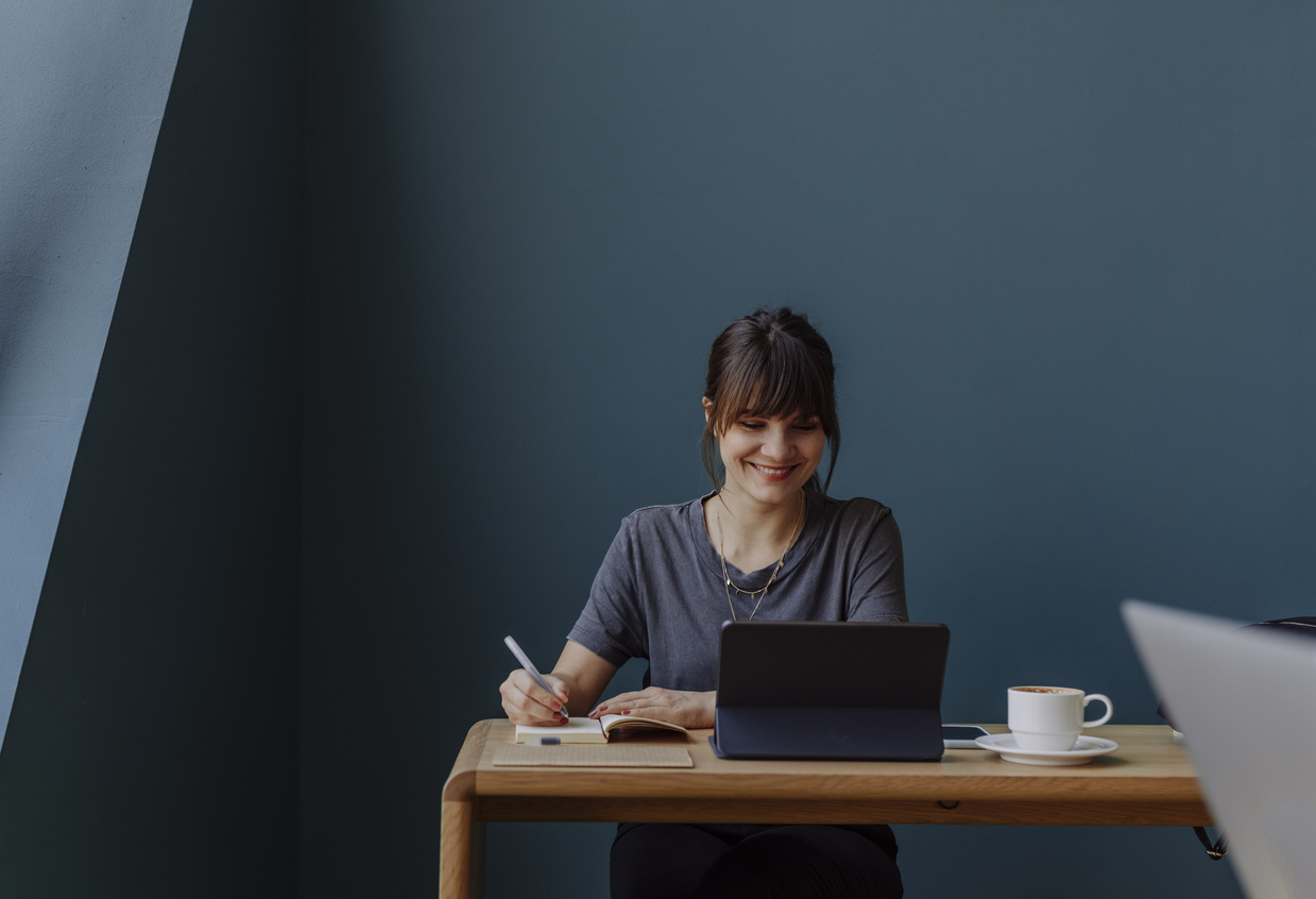 Happy young woman, casually dressed, using technology at work (blue background, copy space).